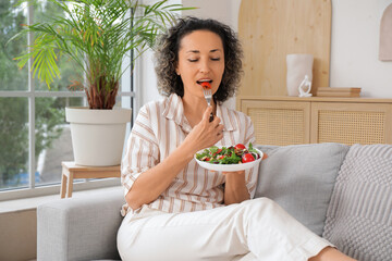 Mature woman eating vegetable salad on sofa at home