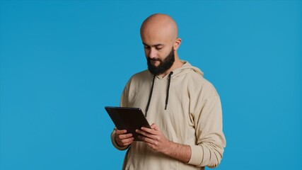 Arab guy using tablet to scroll on online websites, looking for something on the internet and using social media apps. Modern person working with touchscreen device in studio. Camera 1.