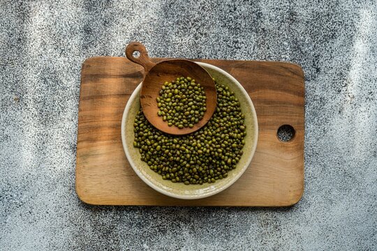 Overhead view of a bowl of raw mung beans on a wooden chopping board