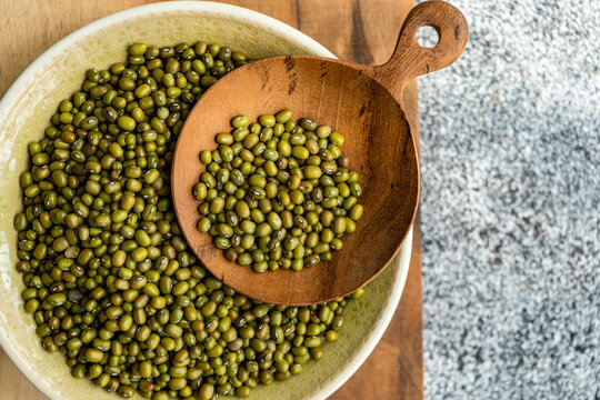 Overhead view of a bowl of raw mung beans (Vigna radiata) on a wooden chopping board