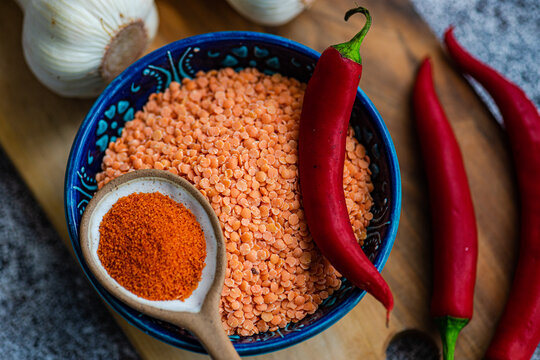 Overhead view of a bowl of red lentils, red chilli peppers, chilli powder and garlic on a wooden chopping board