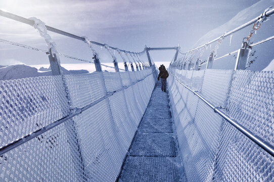 Distant rear view of a man walking across Titlis Cliff Walk suspension bridge, Engelberg, Switzerland