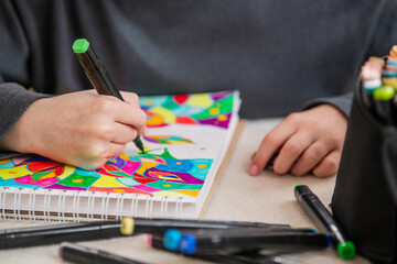 A person is drawing a colorful picture with markers on a piece of paper.