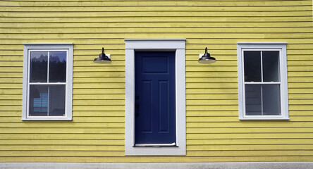 Facade of yellow clapboard house with door and two windows