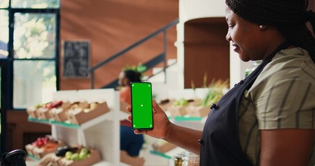 African american vendor holding phone with greenscreen, presenting isolated chromakey layout on...