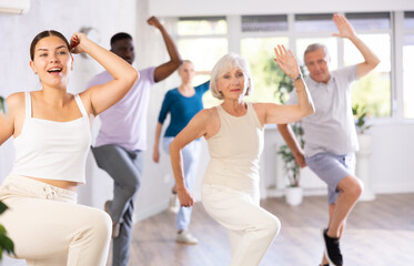 Fototapeta premium Energetic young girl dance instructor conducting class for mixed age group of adults, practicing modern vigorous dance movements