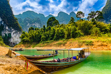 Naklejka premium Wooden longtail boats on the shore of a lake surrounded by rainforest and cliffs (Khao Sok National Park)