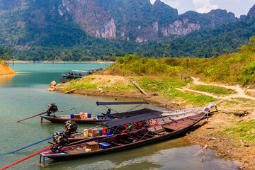 Wooden longtail boats on the shore of a lake surrounded by rainforest and cliffs (Khao Sok National...