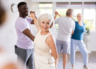 Active mature men and women practicing Ballroom dances in training hall during dancing classes