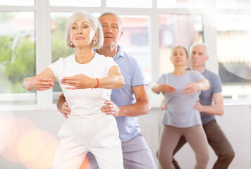 Gracious old woman doing plie position in pair with man during choreography classes in dance studio