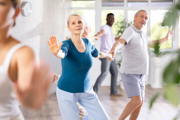 Active mature men and women practicing Rock 'n' Roll dance in training hall during dancing classes