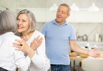 Obraz premium Two elderly woman greet each other by kissing each other on the cheek. While the men shake hands