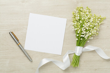 Lilies of the valley with notebook on wooden background, top view