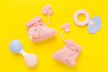 Pink baby booties and rattles on color background, top view
