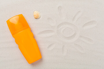 Sunscreen lotion with summer decor on sand background, top view
