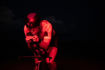 Obraz premium A triathlete rides his bike in the darkness of night, pushing himself to prepare for a marathon. The contrast between the darkness and the light of his bike creates a sense of drama and highlights the