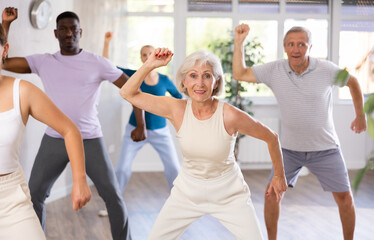 Fototapeta premium Elderly woman and small group of amateur dancers of different ages are actively engaged in fitness room. Physical activity, good bodily shape