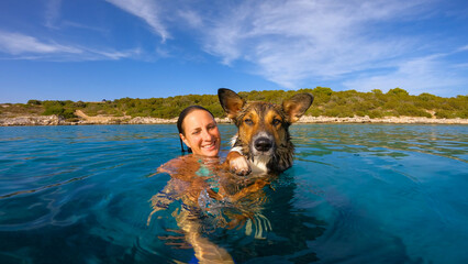 PORTRAIT, CLOSE UP: Smiling lady holds her cute dog as they float and swim in the incredibly blue...