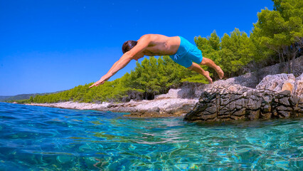 LOW ANGLE VIEW: Carefree vacationer jumps head first into crystal clear seawater at Dalmatian...
