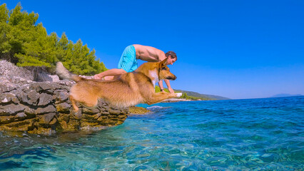 LOW ANGLE VIEW: Brown dog and young man simultaneously jump head first into refreshing crystal...