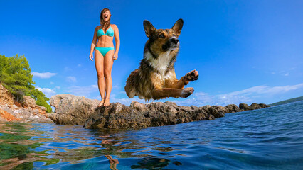 LOW ANGLE VIEW: Doggo caught in the air while jumping in refreshing blue sea with a lady in bikini...