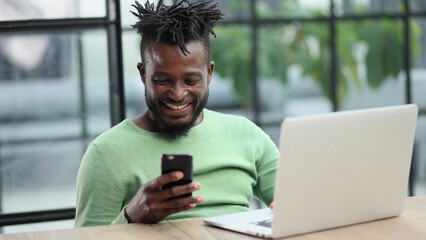 Black businessman talking on a mobile phone in the office while using a laptop