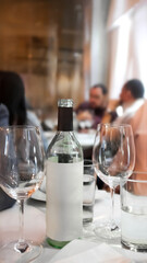 A bottle of wine sits on a table of a restaurant with two wine glasses and a cup of water
