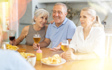 Group of happy seniors celebrating holiday drinking and chatting at table at home