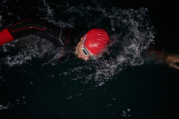 A determined professional triathlete undergoes rigorous night time training in cold waters, showcasing dedication and resilience in preparation for an upcoming triathlon swim competition