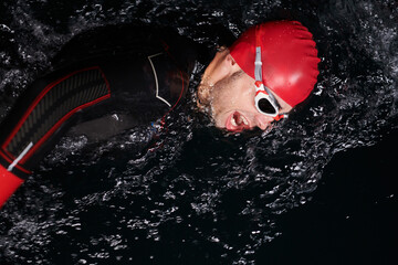 A determined professional triathlete undergoes rigorous night time training in cold waters,...