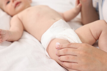 Woman applying body cream onto baby`s skin on bed, closeup