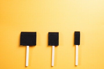 Foam sponge paint brush, black with wooden handle, yellow background.