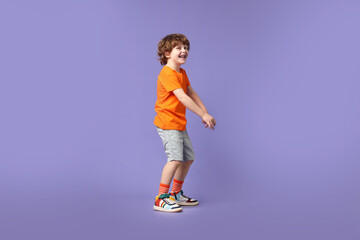 Happy little boy dancing on violet background