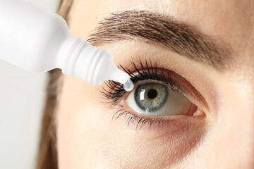 Woman applying eye drops on light background, closeup