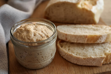 Sourdough starter in glass jar and bread on table, closeup