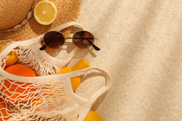 String bag with sunglasses, straw hat and fruits on beige textured background, flat lay. Space for...