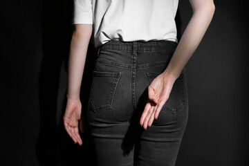 Woman showing open palm behind her back on black background, back view
