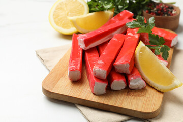 Tasty crab sticks, pieces of lemon and parsley on white table, closeup
