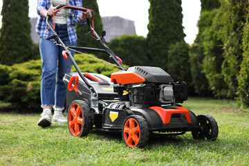 Woman cutting green grass with lawn mower in garden, selective focus