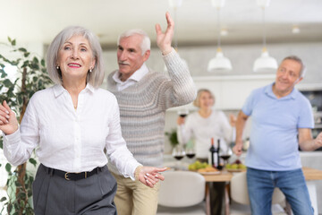 Two married couples pensioners dance during holiday, have fun, move and jump in dining room. Family...