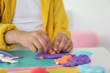 Little girl sculpting with play dough at table indoors, closeup