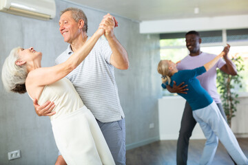 Active mature men and women practicing Ballroom dances in training hall during dancing classes