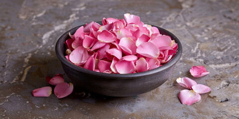 Pink rose petals are in a bowl on a concrete floor.