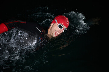 A determined professional triathlete undergoes rigorous night time training in cold waters, showcasing dedication and resilience in preparation for an upcoming triathlon swim competition