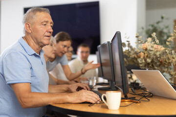 Elderly man taking computer lessons with group of elderly people in a nursing home