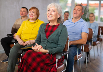 Positive interested elderly woman listening attentively and taking notes on lesson during language...