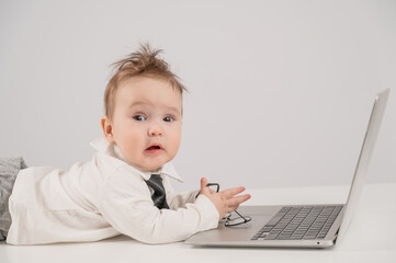 Cute baby boy in a tie working at a laptop. 