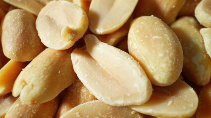 A close-up reveals the allure of roasted peanuts, golden-brown and glistening, their halves unveil a smooth, oily interior. Each with its distinct two-lobed shape, promising crunchy delight.
