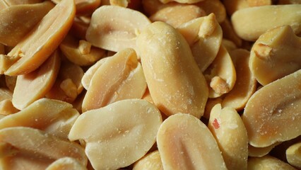 A detailed close-up unveils roasted peanuts, their split halves, lightly salted surfaces, and a spectrum of shades from light tan to deep brown, epitomizing their crunchy essence.
