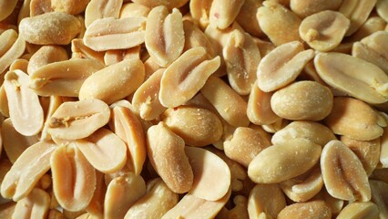 A close-up reveals golden-brown roasted peanuts, split open to expose their creamy kernels. Their rough texture glistens under light, adorned with a delicate dusting of salt.
